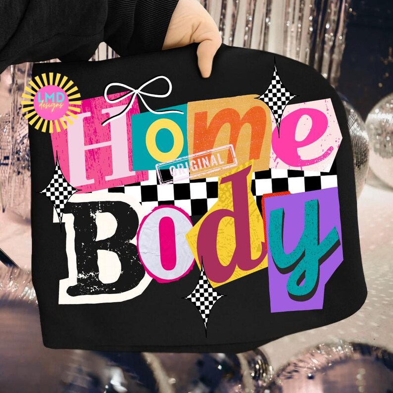 May include: Black tote bag with the words "Home Body" in a collage style. The letters are in various colors, including pink, orange, and teal, with a white bow and checkered accents. The bag has a "LMD designs" logo.