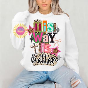 May include: White sweatshirt with the phrase "His Way Is Better" in a colorful, layered design. The design includes leopard print, stars, and a cross. The sweatshirt has a crew neck and long sleeves.