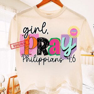 May include: Cream-colored t-shirt with the words "girl. PRAY Philippians 4:6" in black, orange, pink, and teal. The word "ORIGINAL" is stamped on the left side. A sunburst logo is on the right.