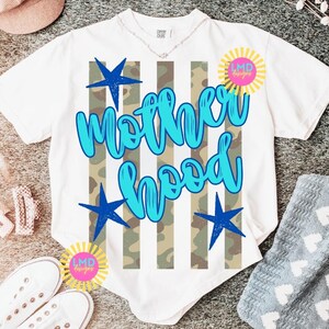May include: White t-shirt with the word "Motherhood" in blue script, accented with blue stars and a camouflage stripe design. The shirt also features a sunburst logo with the text "LMD designs".