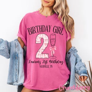 Może przedstawiać: R&oacute;żowa koszulka urodzinowa z napisem "Birthday Girl" i r&oacute;żową cyfrą 21 z kieliszkiem szampana. Pod cyfrą znajduje się napis "Lauren's 21st Birthday Nashville, TN".