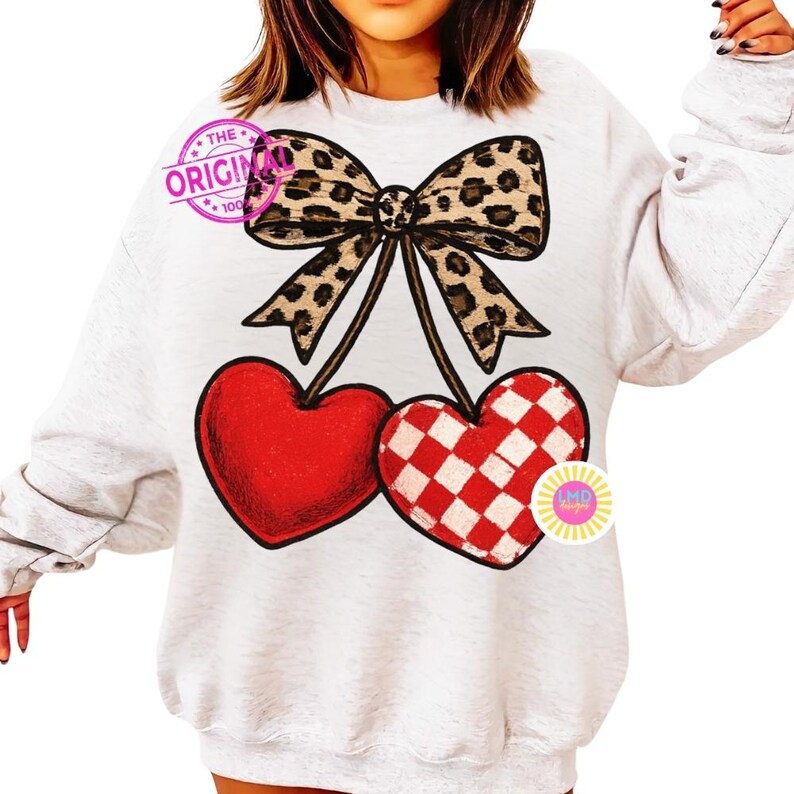 May include: A light gray sweatshirt featuring a large leopard print bow above two heart-shaped cherries. One cherry is solid red, and the other has a red and white checkered pattern. The text "THE ORIGINAL" is visible.