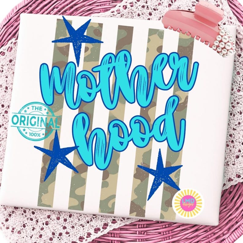 May include: A white canvas with the words "Motherhood" in turquoise script, accented with blue stars and a camouflage stripe design. The phrase "The Original 100%" is also visible. A pink hair clip is on the top right.