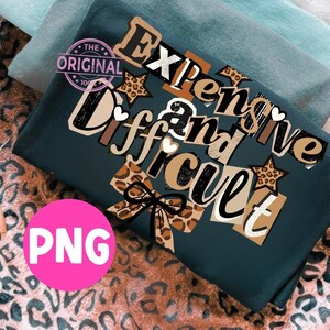 Pu&ograve; includere: T-shirt verde scuro con la scritta "Expensive and Difficult" in un mix di font e motivi, tra cui stampa leopardata e stelle. Un cerchio rosa con "PNG" &egrave; nell'angolo in basso a sinistra. Il logo originale &egrave; nell'angolo in alto a sinistra.
