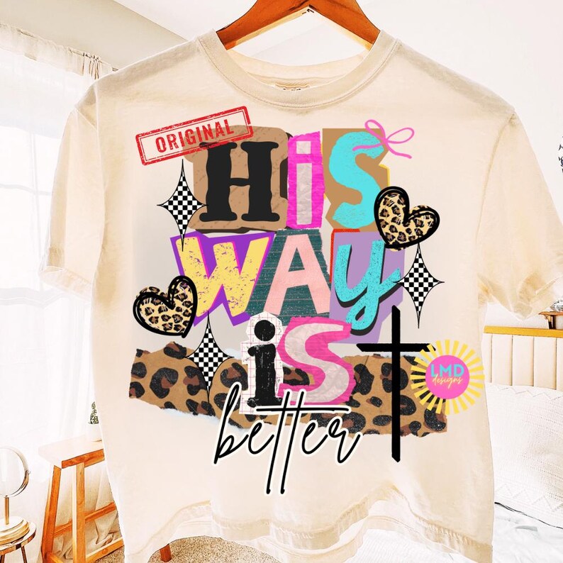 May include: Cream-colored t-shirt with a colorful graphic design. The design includes the words "His Way is better" in various fonts and colors, along with a cross, hearts, and stars. The word "Original" is in a red rectangle.