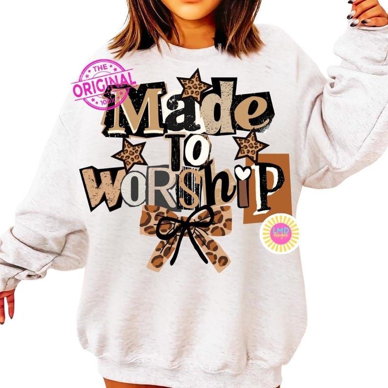 K&ouml;nnte beinhalten: Ein hellgraues Sweatshirt mit dem Schriftzug "Made to Worship" in verschiedenen Schriftarten und Farben. Das Design umfasst Sterne und Schleifen mit Leopardenmuster. Ein rosa Stempel mit der Aufschrift "The Original" ist oben links zu sehen.