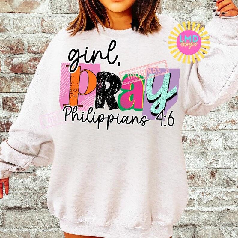 May include: White sweatshirt with the words "girl. PRAY Philippians 4:6" in a colorful, layered design. The word "PRAY" is in black, orange, pink, and teal. The sweatshirt has long sleeves and a crew neck.