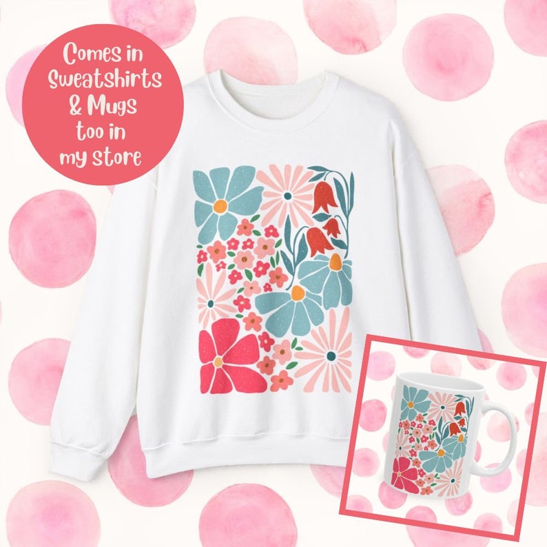 K&ouml;nnte beinhalten: Wei&szlig;er Pullover mit einem farbenfrohen Blumendesign. Das Design zeigt rosa, rote, blaue und gr&uuml;ne Blumen. Der Pullover wird neben einer wei&szlig;en Tasse mit dem gleichen Blumendesign gezeigt. Der Text "Comes in Sweatshirts & Mugs too in my store" ist in einem rosa Kreis oben links im Bild geschrieben.
