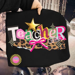 May include: Black tote bag with the word "Teacher" in a colorful, cut-out style. Features a gold star, a pink bow, and a leopard print section. The word "ORIGINAL" is also visible.