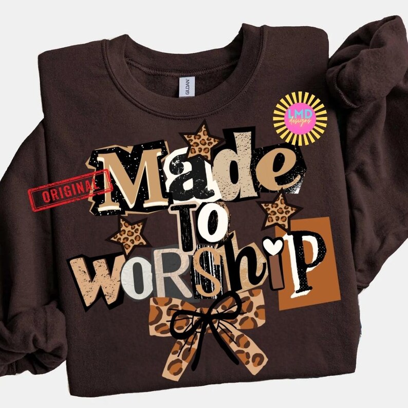 K&ouml;nnte beinhalten: Ein braunes Sweatshirt mit dem Schriftzug "Made to Worship" in einem mehrschichtigen Design. Das Design umfasst Leopardenmuster-Sterne und eine Schleife, mit dem Wort "Original" links gestempelt.