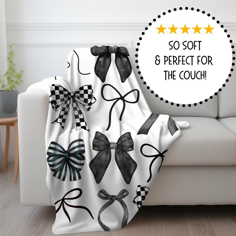 May include: White fleece throw blanket with a black and white bow pattern. The blanket is folded and draped over a white couch.