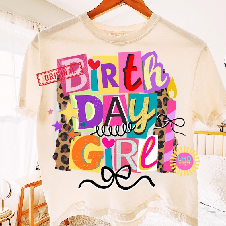 May include: Cream-colored t-shirt with a colorful "BIRTHDAY GIRL" graphic. The design features the text in various colors, leopard print accents, candles, stars, and bows. The word "ORIGINAL" is stamped on the upper left.