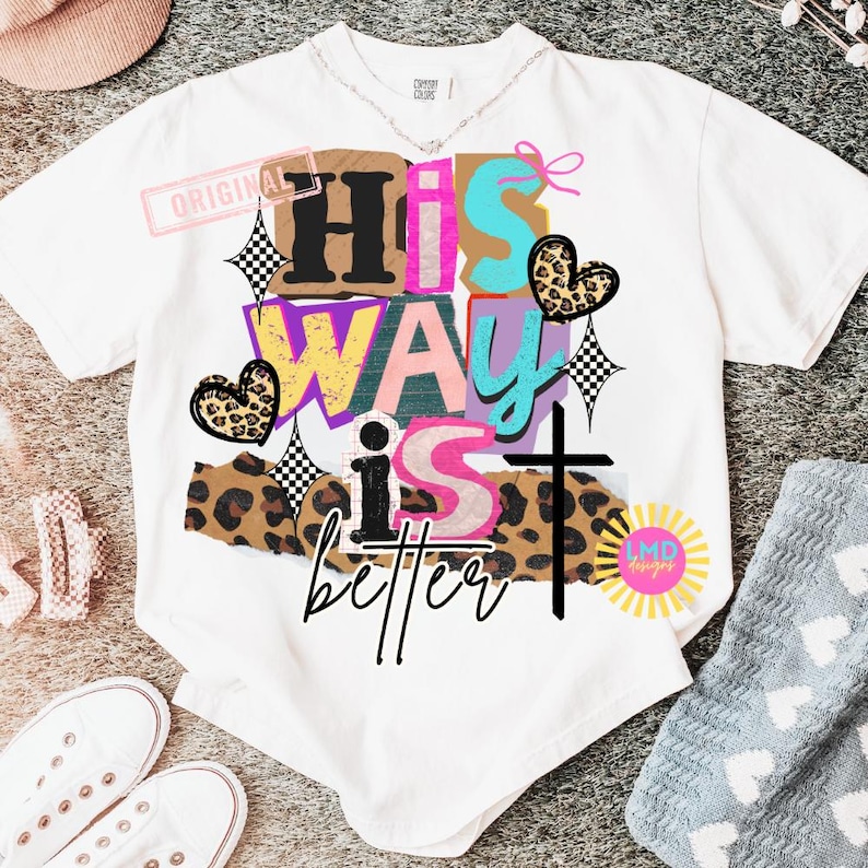 May include: White t-shirt with the phrase "His Way is Better" in a colorful, layered design. The design includes a cross, hearts, and checkered elements. The shirt has a crew neck and short sleeves.