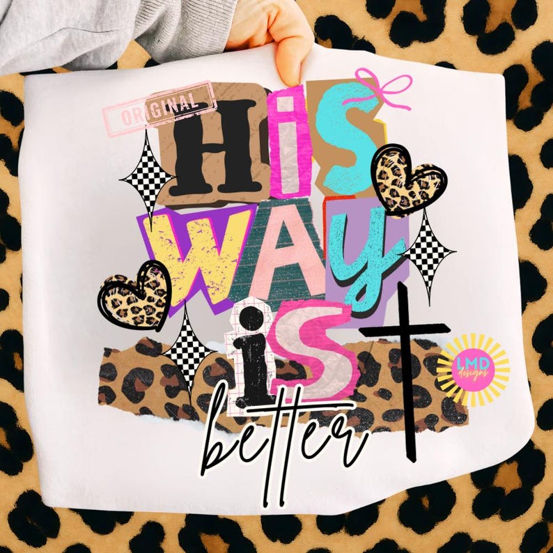 May include: White graphic tee with the text "HIS WAY IS better" in a colorful, layered design. The design includes a cross, hearts, and a leopard print pattern. The word "ORIGINAL" is stamped in pink.