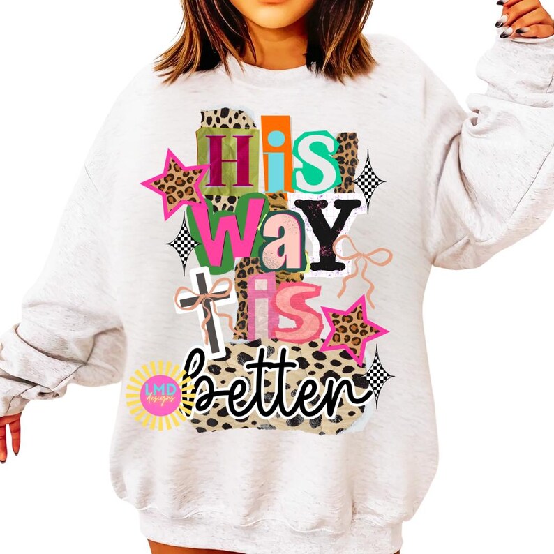 May include: A light gray sweatshirt with the text "His Way Is Better" in a colorful, layered design. The design includes stars, a cross, and leopard print accents. The sweatshirt has long sleeves.