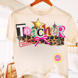 May include: Cream-colored t-shirt with the word "Teacher" in a colorful, layered design. The design includes a gold star, a pink bow, and a leopard print section. The word "ORIGINAL" is stamped on the shirt.