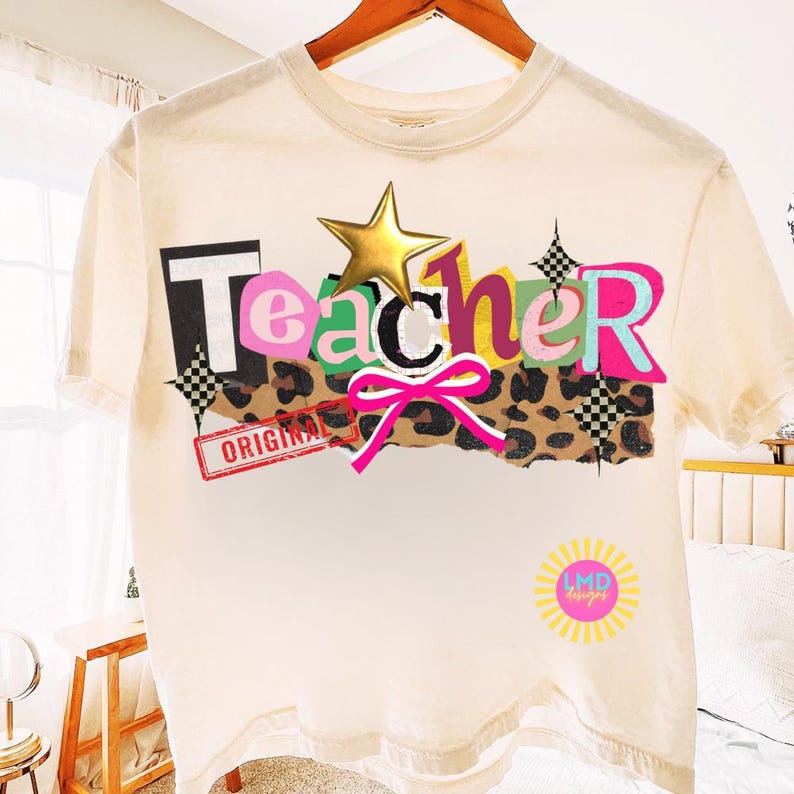 May include: Cream-colored t-shirt with the word "Teacher" in a colorful, layered design. The design includes a gold star, a pink bow, and a leopard print section. The word "ORIGINAL" is stamped on the shirt.