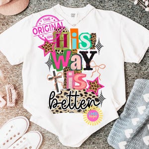 May include: White t-shirt with a colorful graphic that reads "His Way Is Better." The design includes leopard print, stars, and a cross. A pink stamp says "The Original 100%."