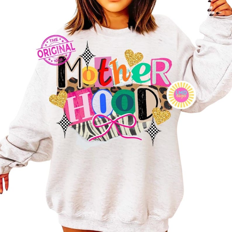 May include: A light gray sweatshirt with the word "Motherhood" in colorful, layered text. The design includes gold glitter hearts, a zebra print, and a pink bow. The words "The Original" are stamped on the upper left.