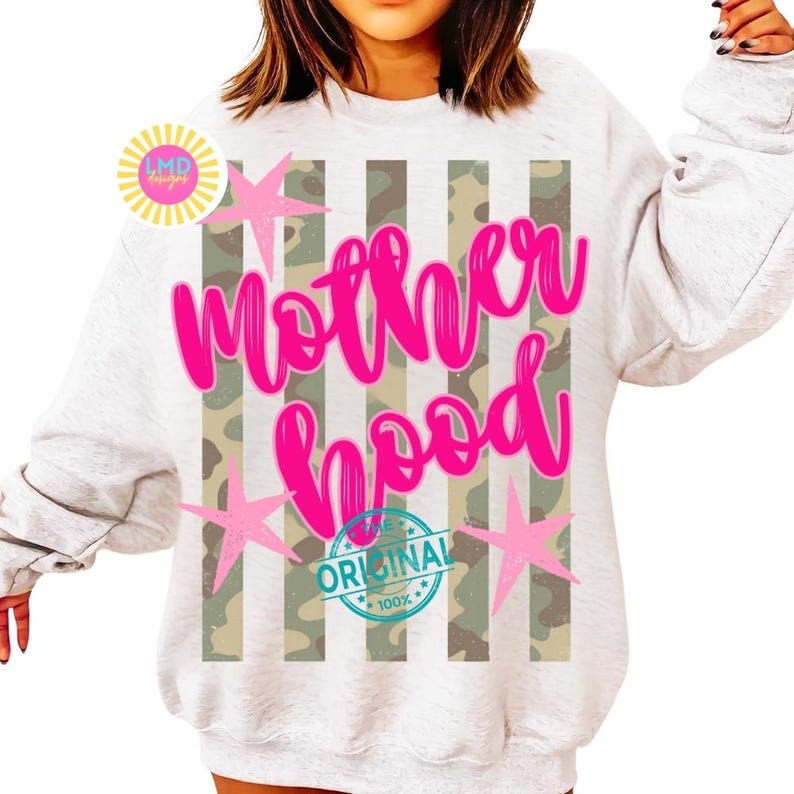 May include: A light gray sweatshirt with the word "Motherhood" in bright pink script. The design includes a camouflage pattern and pink star accents. The word "Original" is printed on a blue circle.