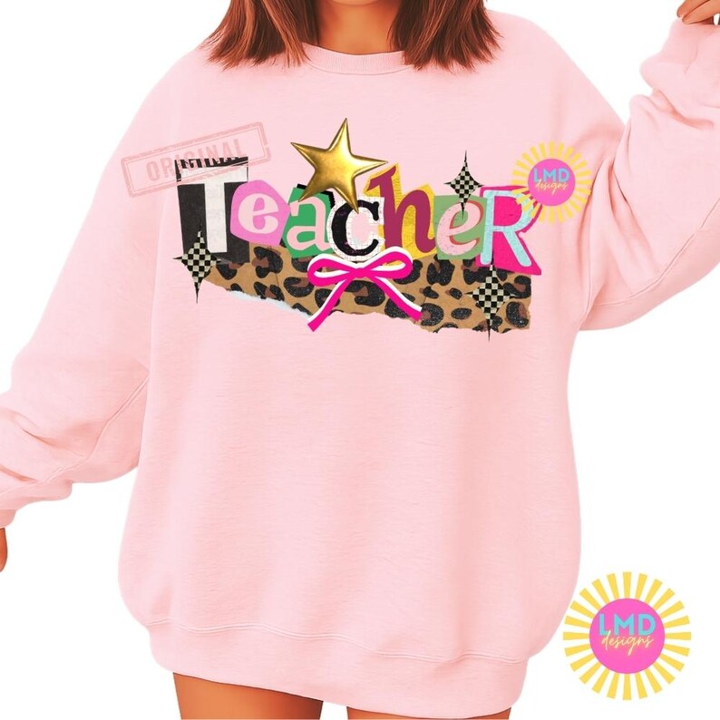 May include: A light pink sweatshirt with the word "Teacher" in a colorful, layered design. The design includes a gold star, leopard print, and a pink bow. The sweatshirt has long sleeves and a crew neck.