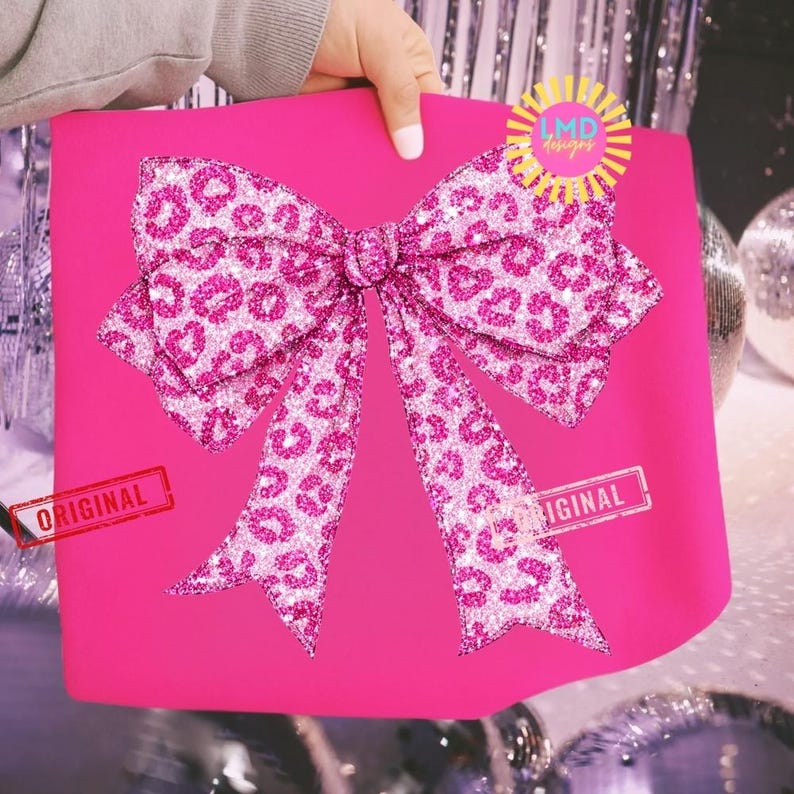 May include: A bright pink gift bag with a large, glittery bow featuring a leopard print design. The bow is centered on the bag, and the image includes the text "ORIGINAL" in a stamp-like design.