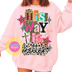 May include: A light pink sweatshirt with the text "His Way Is Better" in a colorful, layered design. The design includes leopard print stars, a cross, and the "LMD designs" logo.