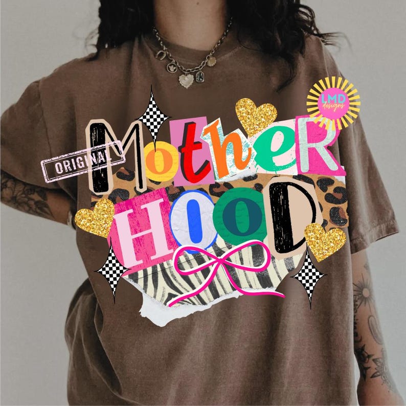 May include: Brown t-shirt with a colorful "Motherhood" graphic. The design incorporates leopard print, zebra stripes, gold glitter hearts, and a pink bow. The word "ORIGINAL" is stamped on the upper left.