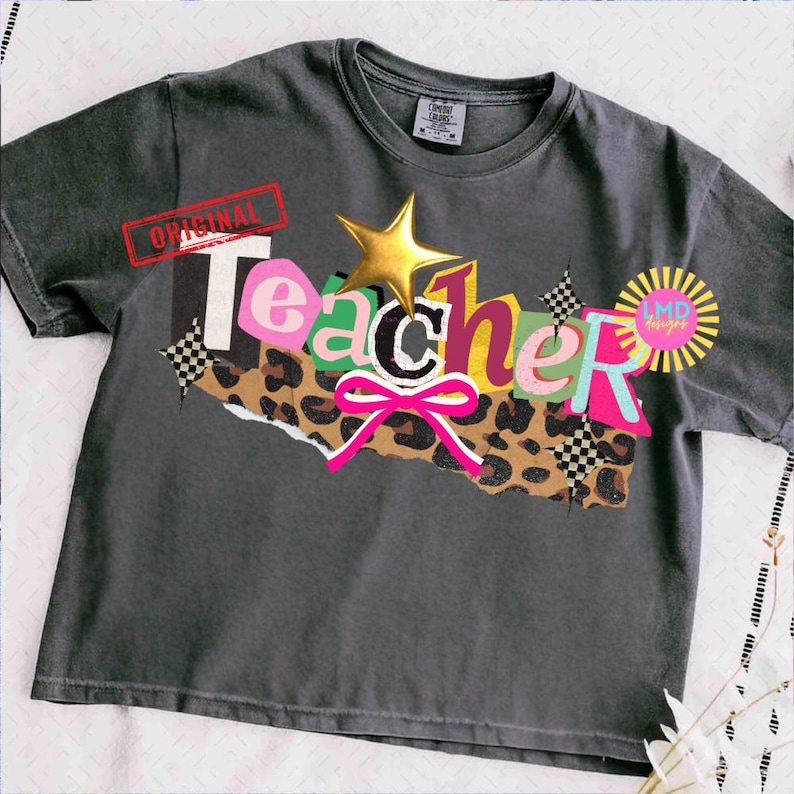 May include: Dark gray t-shirt with the word "Teacher" in colorful, layered letters. The design includes a gold star, a pink bow, and a leopard print section. The word "Original" is stamped in red.