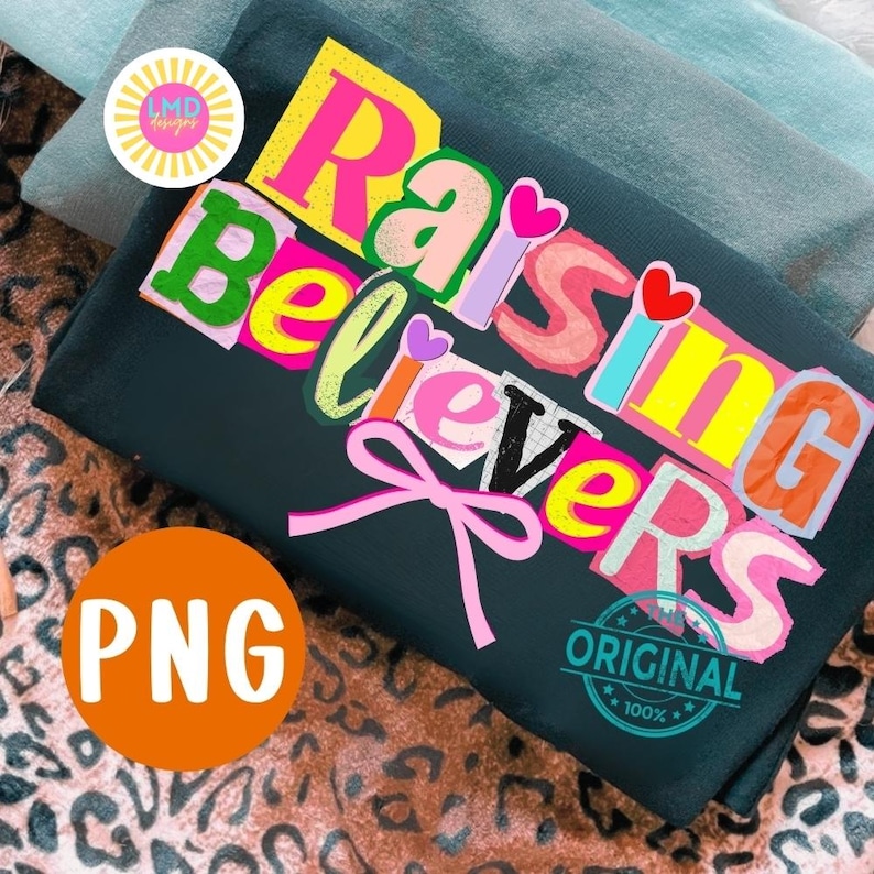 May include: Dark green t-shirt with the words "Raising Believers" in colorful, layered letters. A pink bow is below the text. The shirt has a "PNG" logo and a "Original 100%" stamp.