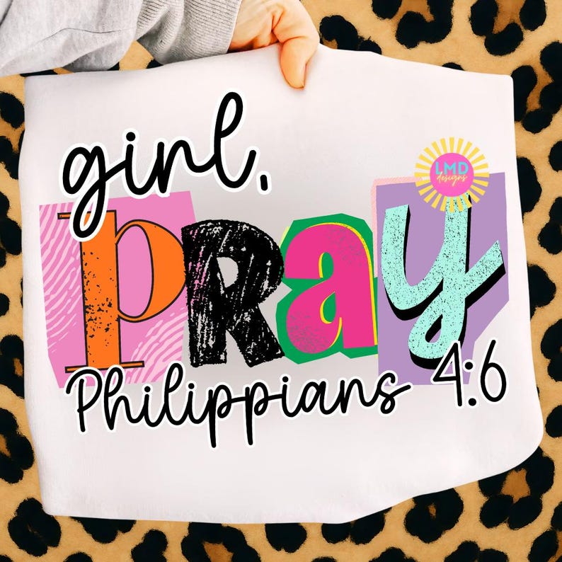 May include: White graphic print featuring the words "girl. PRAY" in various colors and fonts, with "Philippians 4:6" below. The design includes pink, orange, black, green, and blue letters, with a sunburst logo. The background is a leopard print.