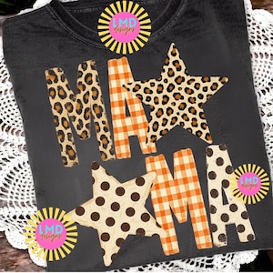 May include: A charcoal grey t-shirt featuring the text MAMA in a mix of patterns. The letters M and A are filled with a brown and black leopard print, while the letters M and A feature an orange and white gingham check pattern. Two large stars are integrated into the design, one with a leopard print and one with brown polka dots. The LMD Designs logo appears in three corners.