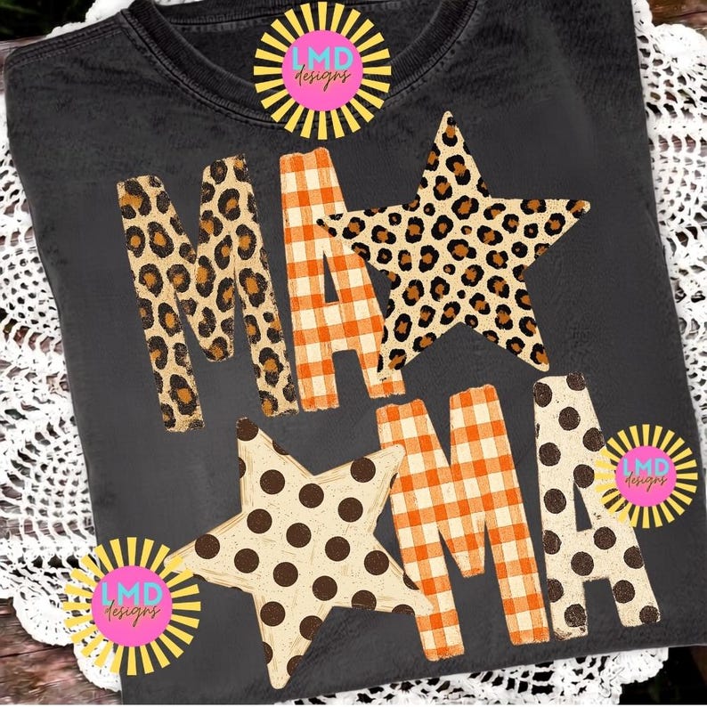 May include: A charcoal grey t-shirt featuring the text MAMA in a mix of patterns. The letters M and A are filled with a brown and black leopard print, while the letters M and A feature an orange and white gingham check pattern. Two large stars are integrated into the design, one with a leopard print and one with brown polka dots. The LMD Designs logo appears in three corners.