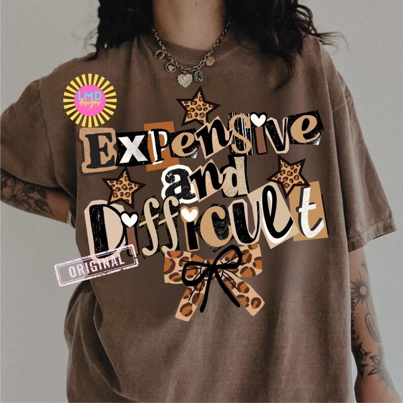 Pu&ograve; includere: T-shirt marrone con la scritta "Expensive and Difficult" in un mix di font e motivi, tra cui stampa leopardata e stelle. La maglietta ha un aspetto vintage e usurato.