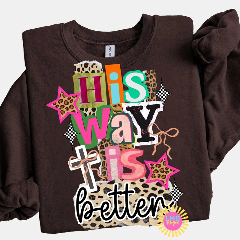 May include: A brown sweatshirt with the phrase "His Way is Better" in a colorful, layered design. The design includes stars, a cross, and leopard print accents. The sweatshirt is a Gildan brand.