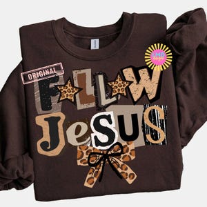 K&ouml;nnte beinhalten: Ein braunes Sweatshirt mit dem Schriftzug "FOLLOW JESUS" im Collage-Stil. Die Buchstaben haben verschiedene Muster, darunter Leopardenmuster und Sterne. Das Wort "ORIGINAL" ist auf einem rosa Rechteck aufgedruckt. Unten befindet sich eine Schleife mit Leopardenmuster.