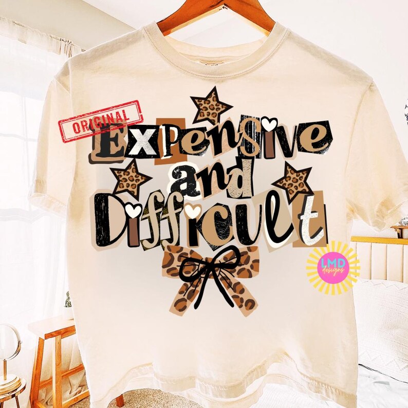 Pu&ograve; includere: T-shirt color crema con le parole "Expensive and Difficult" in stile collage. Il design include stelle e un fiocco con stampa leopardata, con la parola "Original" stampata in alto a sinistra.