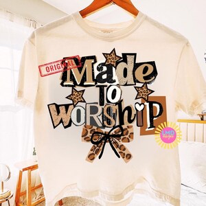 K&ouml;nnte beinhalten: Cremefarbenes T-Shirt mit dem Schriftzug "Made to Worship" in einem mehrschichtigen Design. Das Design umfasst Sterne mit Leopardenmuster und eine Schleife, mit dem Wort "Original" oben links.