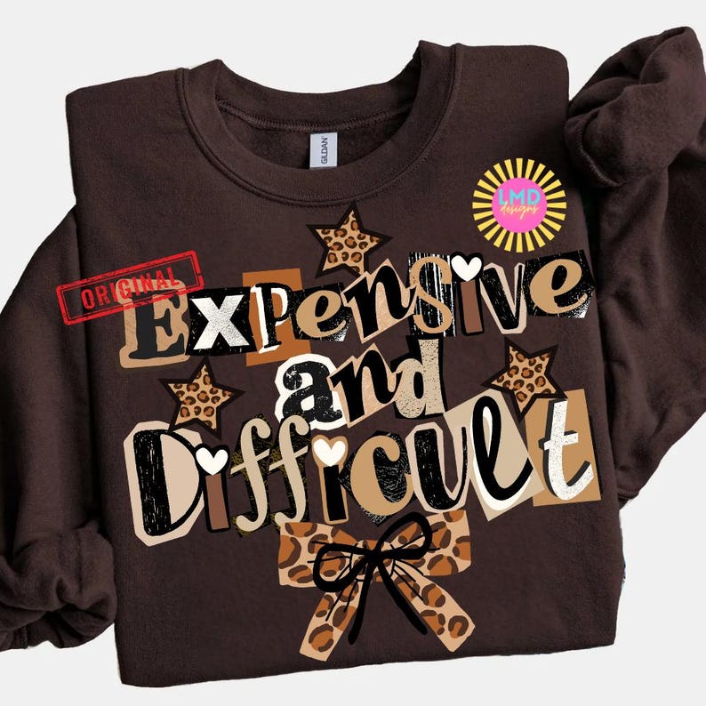Pu&ograve; includere: Una felpa marrone con le parole "Expensive and Difficult" in un design a strati. Il design include stelle con stampa leopardata, cuori e un fiocco. La parola "Original" &egrave; stampata in rosso.