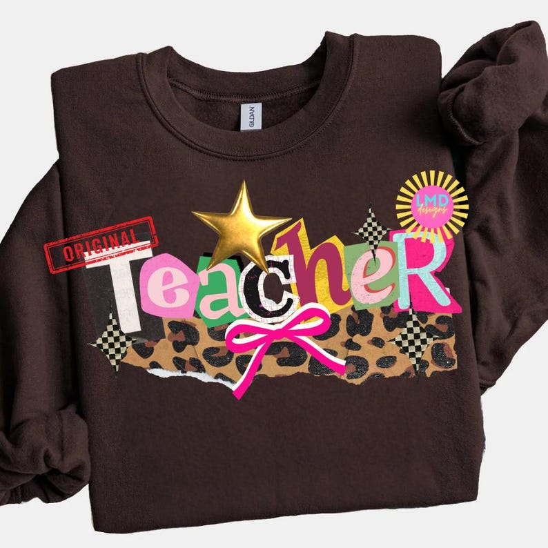 May include: A brown sweatshirt with the word "Teacher" in colorful, layered letters. The design includes a gold star, a pink bow, and a leopard print section. The word "Original" is stamped in red.