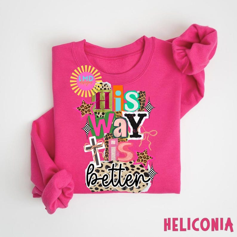 May include: A bright pink sweatshirt with the phrase "His Way Is Better" in a colorful, layered design. The design includes a cross, leopard print accents, and the text "HELICONIA" at the bottom.