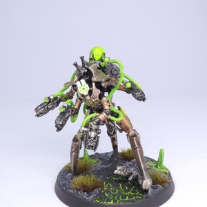 May include: A detailed, painted miniature of a robotic figure with a green head and glowing green accents. The figure is posed on a black base with green accents and textured ground.