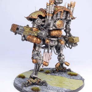 May include: A detailed model of a war machine, featuring a metallic silver body with bronze and olive green accents. The model stands on a textured base with faux grass and a painted path. It has a large weapon and intricate mechanical details.