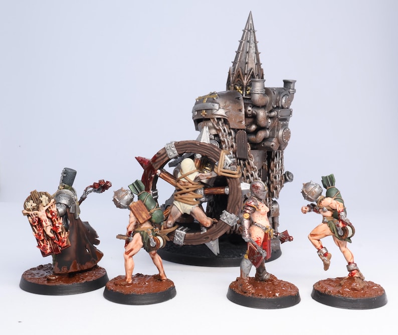 Puede incluir: Figuras en miniatura que representan una escena de batalla. Las figuras incluyen guerreros con armadura, una estructura central con una parte superior puntiaguda y una rueda de madera. La paleta de colores incluye marr&oacute;n, rojo, plateado y verde.