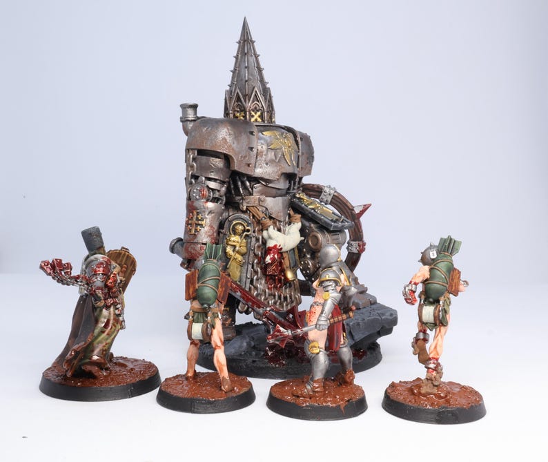 Puede incluir: Un conjunto de figuras en miniatura detalladas, que incluyen una gran m&aacute;quina de guerra met&aacute;lica de estilo g&oacute;tico y varias figuras m&aacute;s peque&ntilde;as en poses de batalla. Las figuras est&aacute;n pintadas con una variedad de colores y texturas, sobre bases marrones.