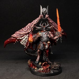 Könnte beinhalten: Eine bemalte Miniaturfigur eines gehörnten Dämons mit großen, gezahnten Flügeln und dunkler Metallrüstung. Die Figur hält ein flammendes orangefarbenes Schwert und ein metallisches Symbol über dem Kopf, stehend auf einem Sockel voller Totenköpfe.