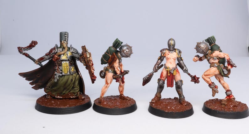 Puede incluir: Cuatro figuras en miniatura de guerreros de fantas&iacute;a. Las figuras est&aacute;n pintadas con armaduras, armas y tonos de piel detallados. Una figura lleva un abrigo largo y lleva una maza y un escudo. Las otras tres figuras est&aacute;n ligeramente blindadas y llevan armas.