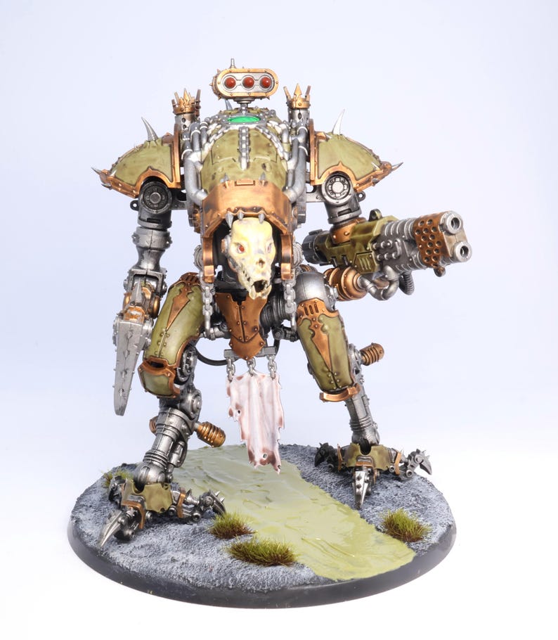 May include: A detailed model of a war machine, featuring a skull-like head and a large gun. The model is painted in shades of green, bronze, and silver, with intricate mechanical details. It stands on a circular base with a painted landscape.