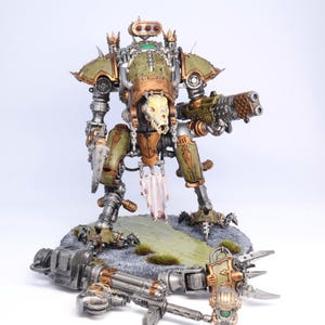 May include: A detailed model of a war machine, featuring a green and bronze color scheme. The model has a skull-like face and is armed with a large gun. It stands on a rocky base with a fallen weapon nearby.