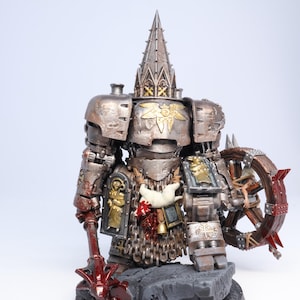 Puede incluir: Figura en miniatura detallada de un guerrero fuertemente blindado. La figura es principalmente met&aacute;lica con detalles dorados, un tocado alto y ornamentado y una rueda con p&uacute;as. La base es gris con detalles rojos, lo que sugiere una escena de batalla.